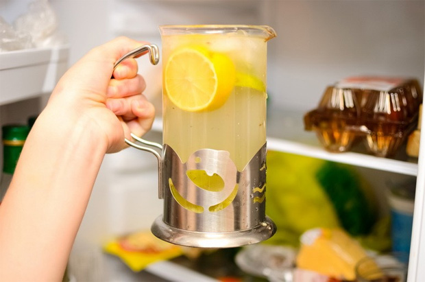 Около открытого холодильника женщина держит в руке кувшин с домашним лимонадом