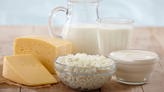 На столе стоят молочные продукты, сыр, творог, сметана и молоко в графине