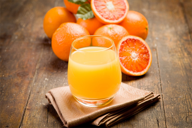 На деревянном столе несколько апельсинов и стакан с апельсиновым соком