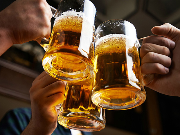 Трое мужчин в баре чокаются полулитровыми кружками с пенными пивом