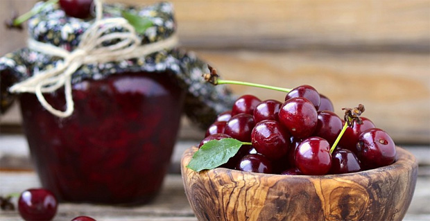 На столе стоит баночка с вишневым вареньем и вазочка со свежей ягодой