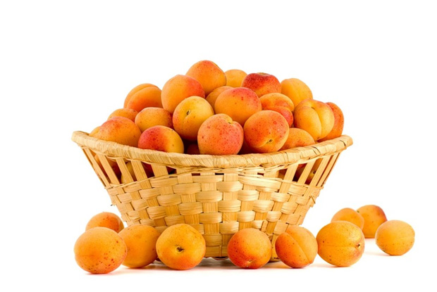 В плетеной вазе и рядом с ней много ягод спелого абрикоса