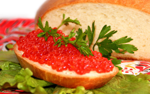На столе буханка белого хлеба и бутерброд с красной икрой на листе салата