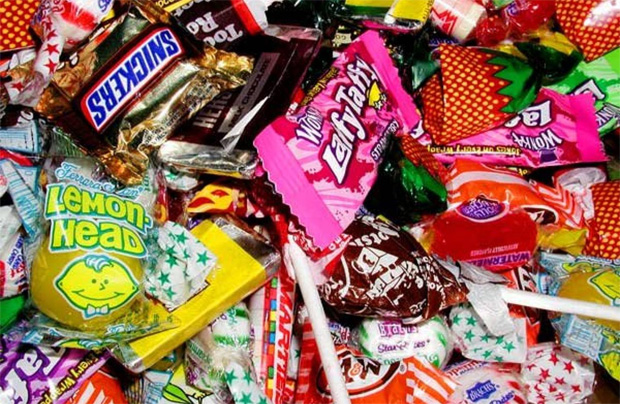 На столе большая россыпь различных брендовых конфет в заводской упаковке