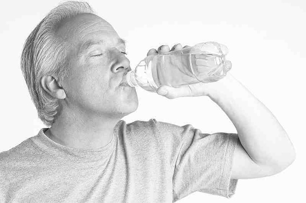 Мужчина испытывает сильную жажду и пьет воду из пластиковой бутылки