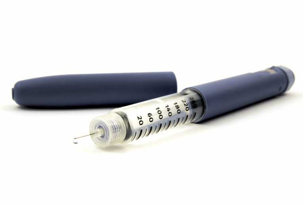На белой поверхности лежит открытая ручка шприц с капелькой инсулина на игле