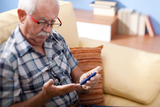 Пожилой мужчина с седыми усами и в очках измеряет прибором уровень сахара в крови