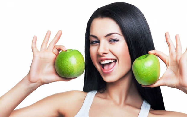 Улыбающаяся девушка с темными волосами держит в руках два зеленых яблока