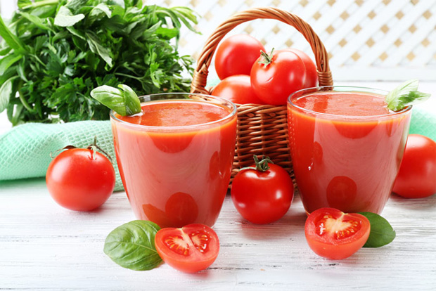 На столе два стакана с томатным соком, корзина с помидорами и зелень