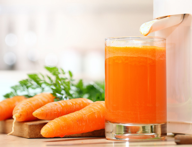Около соковыжималки стоит стакан с морковным соком и рядом лежит морковь
