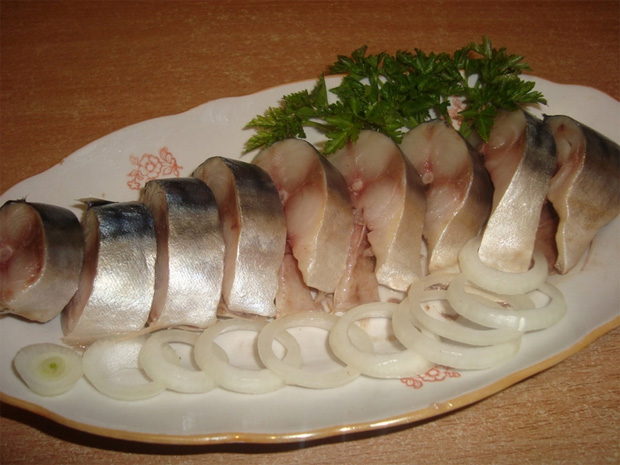 На блюдо для рыбы выложена нарезанная сельдь с кружочками репчатого лука