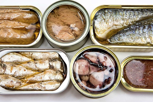 На столе несколько видов рыбных консервов в заводских банках от производителя