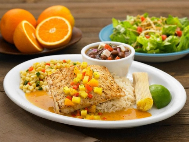 На столе тарелка со сбалансированным полезным блюдом, апельсины и миска с салатом