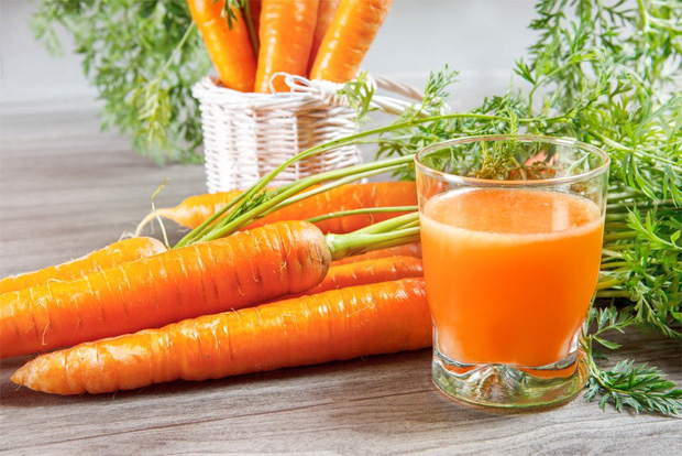 На столе лежит несколько корнеплодов моркови и стоит стакан с морковным соком