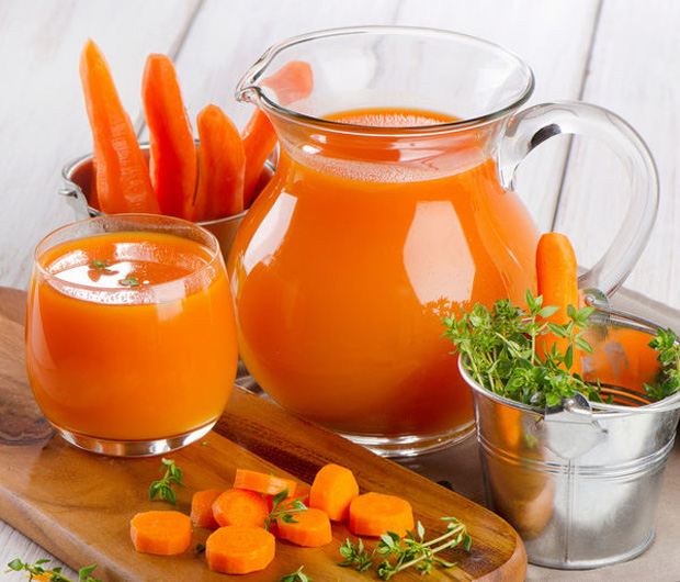 На столе кувшин и стакан с морковным соком на фоне нарезанной и целой моркови