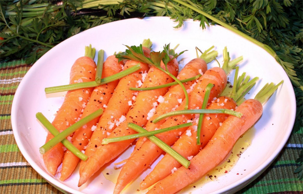 На белой тарелке выложены корнеплоды моркови, посыпанные приправой и зеленью