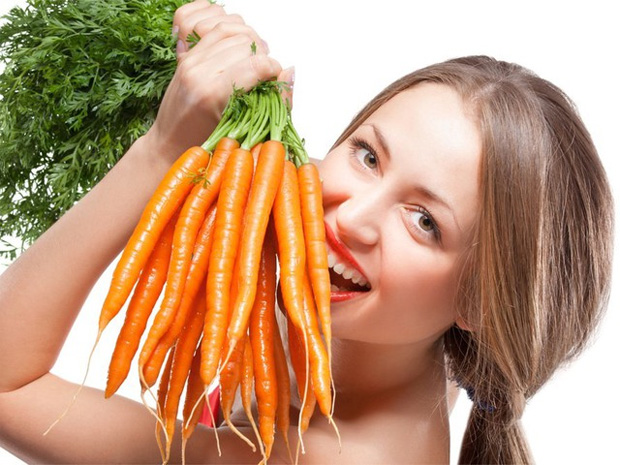 Девушка на уровне лица держит большую связку молодой моркови