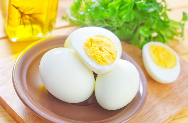 На бежевой тарелке лежит три вареных вкрутую куриных яйца и зелень