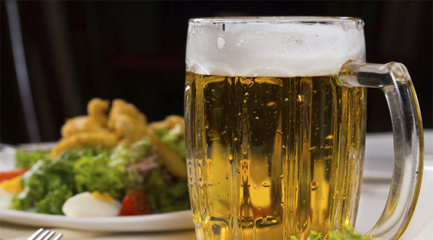 На фоне блюда с приготовленной едой стоит кружка со светлым пивом
