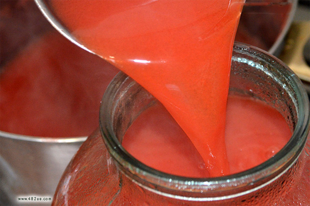 На кухне человек выливает в трехлитровую банку свежевыжатый томатный сок