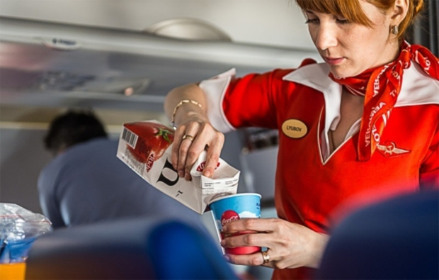 Стюардесса в самолете наливает пассажиру томатный сок в бумажный стакан