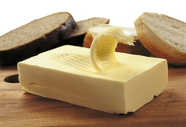 На разделочной доске на фоне нарезанного хлеба лежит брусок сливочного масла