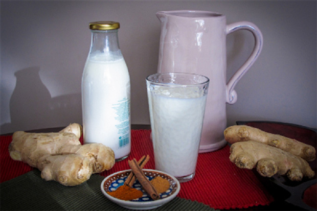 На столе стоит бутылка и стакан с кефиром, графин, два корня имбиря и блюдце с корицей