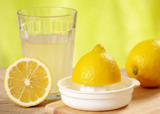 На столе стоит стакан с лимонным соком, разрезанный фрукт и соковыжималка