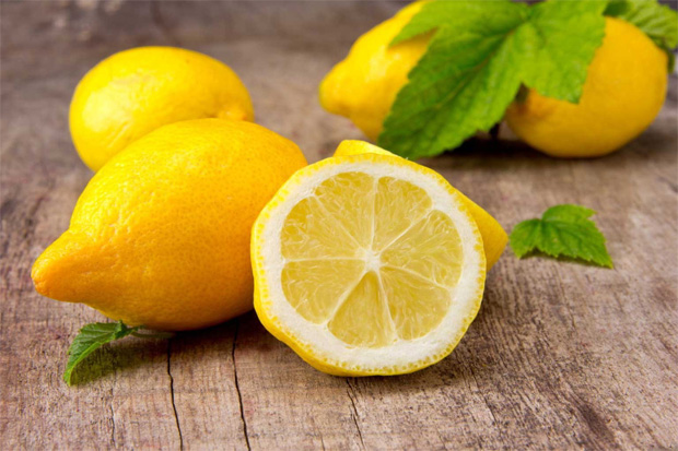 На деревянном столе лежит несколько плодов лимона, один из них в разрезе