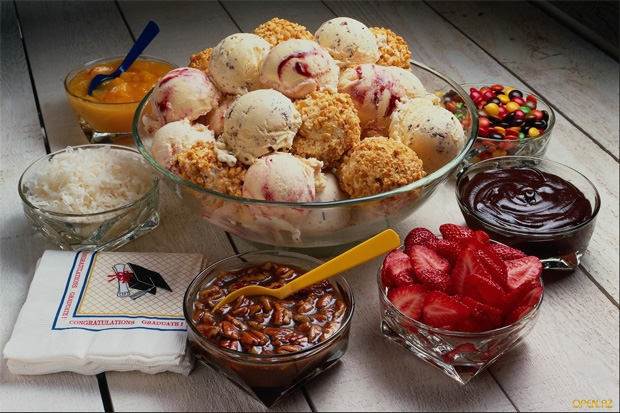 На столе стоит стеклянная ваза с шариками мороженого и различные добавки