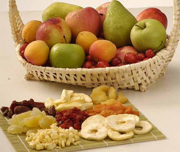 На столе большая корзина со свежими фруктами и бамбуковая салфетка с сухофруктами