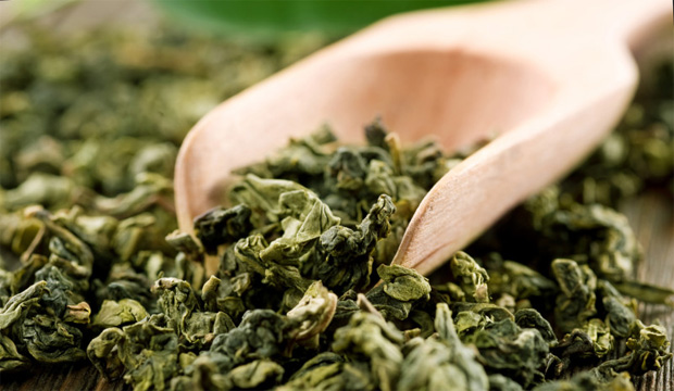 Деревянная лопаточка лежит на россыпи засушенных листьев зеленого чая