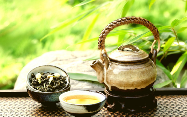 На фоне природы на столе мисочка, заварочный чайник и чашка с зеленым чаем
