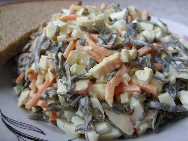 На большом блюде выложен салат из морской капусты, моркови и яблок