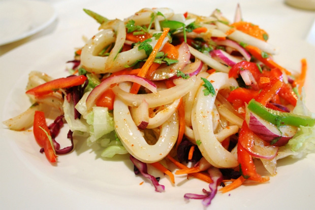 На белой тарелке выложен красивый салат из кальмара и болгарского перца
