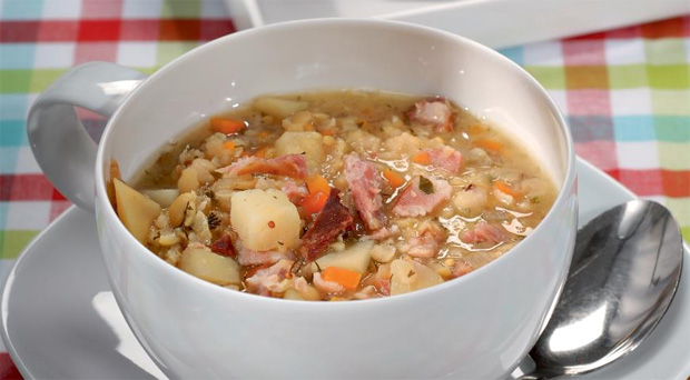 В глубокую белую чашку на блюдце с металлической ложкой налит вкусный суп