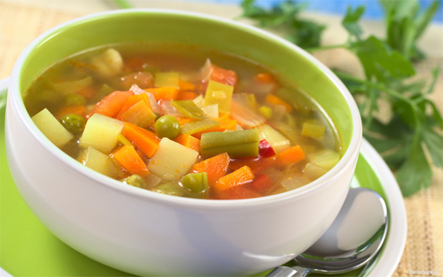 В двухцветной глубокой тарелке с блюдцем суп из овощей на фоне зелени
