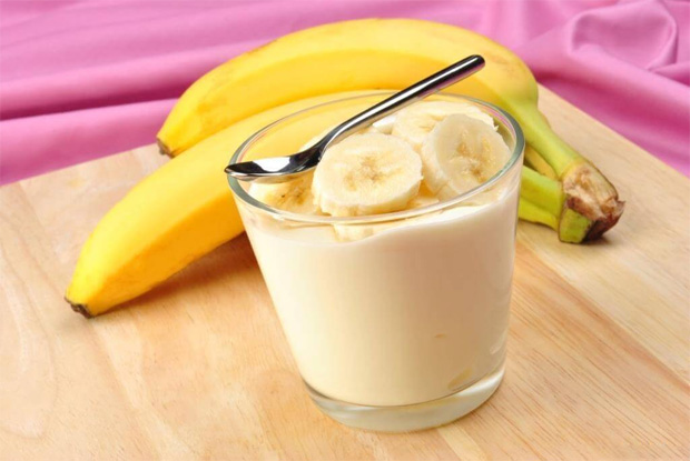 На столе лежат два банана и стоит стакан с молочным продуктом и банананми