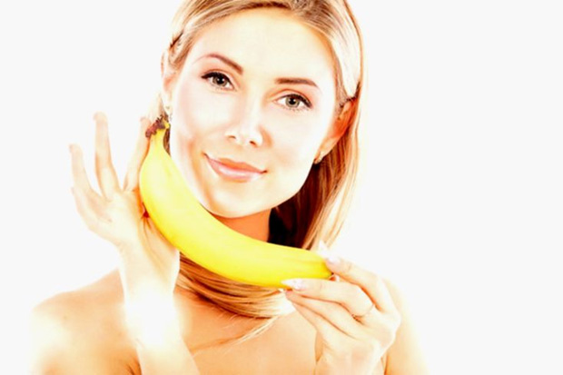 Красивая девушка держит двумя руками банан на уровне лица