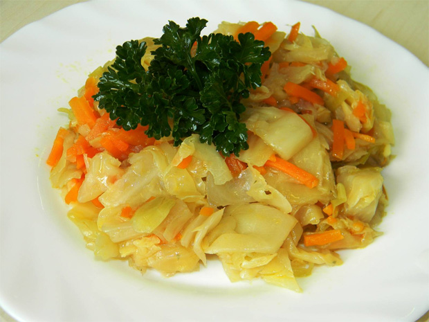 В белой тарелке тушеная капуста кольраби с морковкой и зеленью