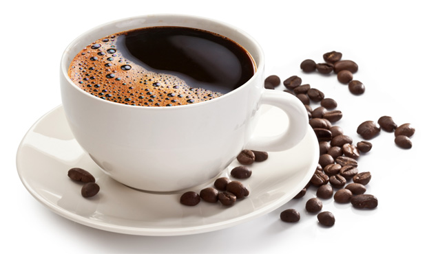 На столе белая чашка с черным кофе на белом блюдце в окружении кофейных зерен