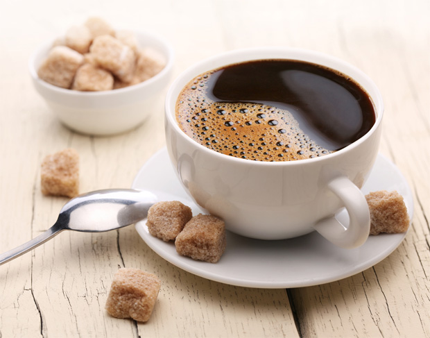 На деревянном столе на блюдце стоит чашка с заваренным кофе и мисочка с кубиками сахара