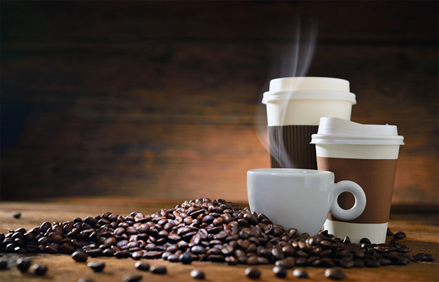 На фоне деревянной стены на столе рассыпаны кофейные зерна и стоят емкости с кофе