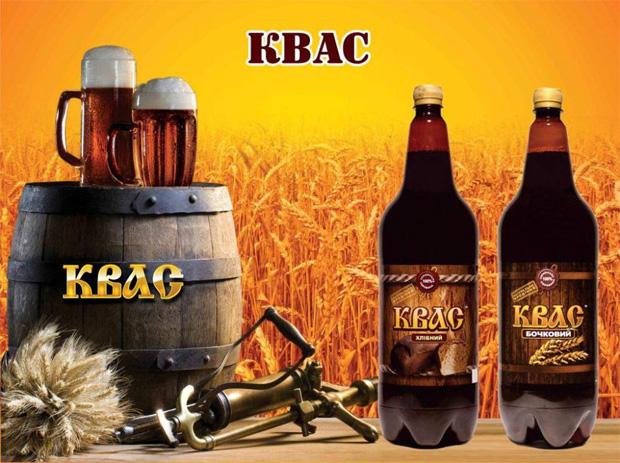 На фоне зрелой пшеницы бочка, две кружки и две бутылки с квасом