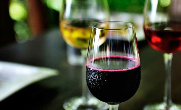 На столе с темной поверхностью стоят три бокала с разными видами вина