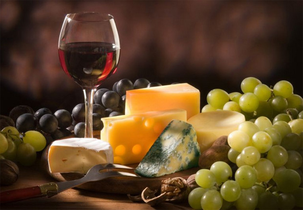 На столе бокал с красным вином, виноград и блюдо с несколькими видами сыра