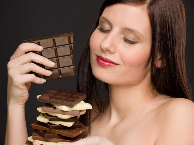 Девушка держит в руке надкусанную плитку шоколада и еще несколько на ладони