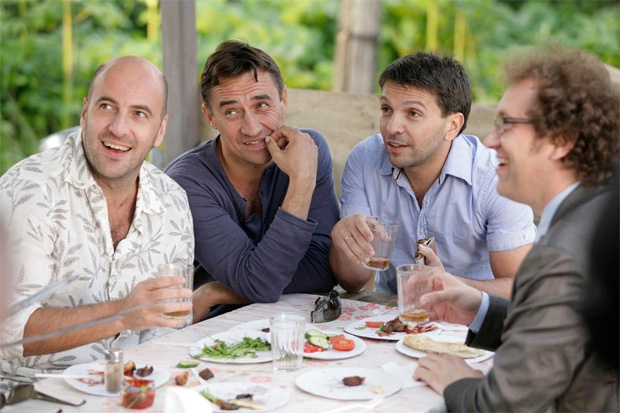 Группа из четырех мужчин сидит на природе и выпивают алкоголь с закуской