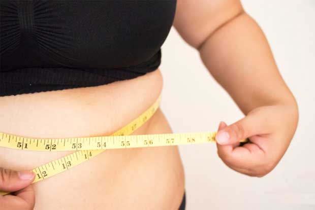 Женщина в черной кофте измеряет лентой размер своей талии при наборе веса