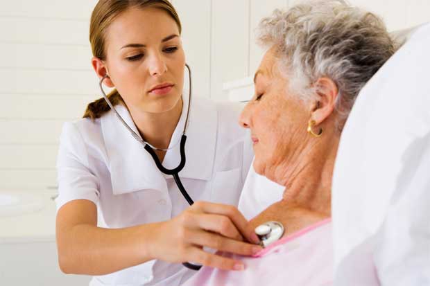 Молодая медсестра слушает стетоскопом стук сердца пожилой пациентки